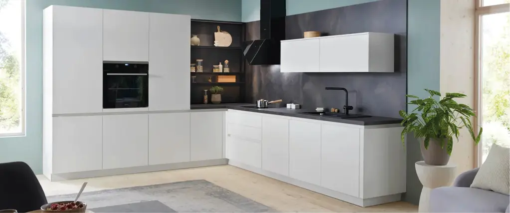 Moderne Einbauküche in Weiß mit L Form, schwarzer Arbeitsplatte und integrierten Elektrogeräten. Minimalistisches Küchendesign mit Oberschränken, offener Regalnische und Pflanzen für zeitgemäßes Wohnen.